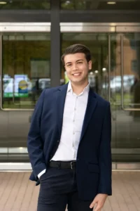 Tarik wearing a light button up shirt and navy jacket. 