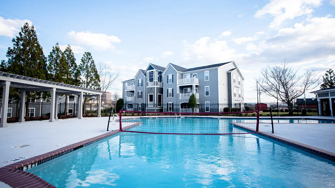 swimming pool with volleyball net and apartment building in the background.
